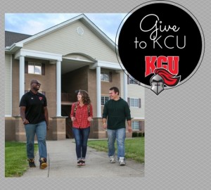 Three people walking and talking in front of a building with columns. A black circle with "To KCU" and a knight helmet logo is on the right side of the image.