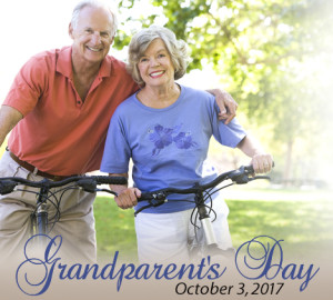 An elderly couple smiling while standing outdoors with bicycles, one wearing an orange shirt and khaki pants, the other in a purple T-shirt and white shorts.