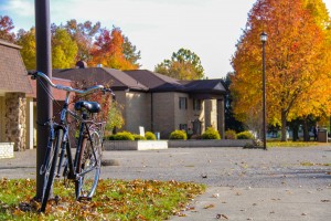 A bicycle is parked near a lamp post in front of a building surrounded by trees with autumn foliage.