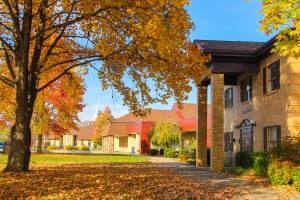 A building with a brick exterior, surrounded by trees with autumn foliage, under a clear blue sky.
