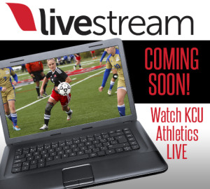 A laptop screen displays a soccer match between players in blue and gold and players in red and black. Text reads, "COMING SOON! Watch KCU Athletics LIVE.