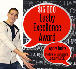A person in casual attire points to a large red speech bubble text that reads "Lusby Excellence Award" offering $15,000. The text also includes that applications are accepted until 4/1/2016.