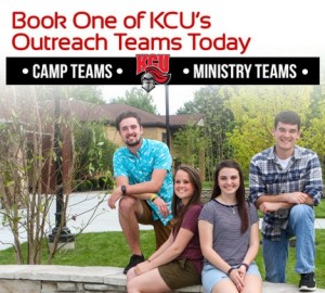Four people are posing and smiling outdoors near a building, with a sign above that reads "KGU Camp Teams Ministry Teams.
