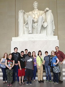 A group of people, proudly showcasing their KCU Degrees, stands in front of the Lincoln Memorial statue, posing for a memorable photo.