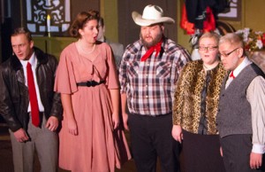 Five people wearing various costumes are standing in a line, performing on stage. The group includes a cowboy, a woman in a pink dress, and individuals in a leather jacket and formal attire, showcasing their talents much like those pursuing diverse KCU Degrees.