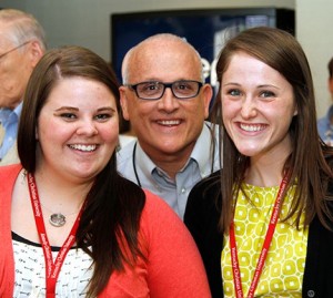 Three people, two women and a man, are smiling at the camera. They are wearing name badges on red lanyards around their necks.