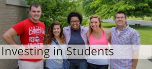 A group of five smiling people stand outdoors, with "Investing in Students" text overlaid on the image.