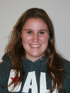 A person with long hair smiles at the camera, wearing a hooded sweatshirt.