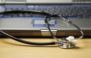 A stethoscope rests on a closed laptop on a wooden surface.