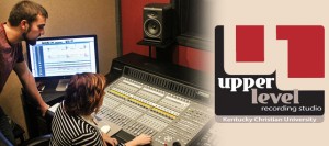 A man and a woman work in a recording studio with audio mixing equipment and a computer. To the right is the "Upper Level Recording Studio" logo of Kentucky Christian University.