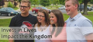 Four young adults stand together smiling outside in a park. Text overlay reads, "Invest in Lives, Impact the Kingdom.