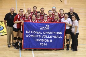 A women's volleyball team poses in a group holding a banner reading "NCCAA National Champions Women's Volleyball Division II 2014" on the gym floor, showcasing the pride of Kentucky Christian University Alumni.