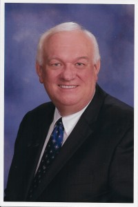 A man, smiling and dressed in a suit with a tie, posed against a blue background. His proud demeanor reflects his distinguished status as Kentucky Christian University Alumni.