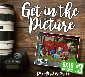 A photo featuring a group of people posed outdoors with large red letters spelling "SITS" on a wooden surface next to a camera lens with the text "Picture" above.