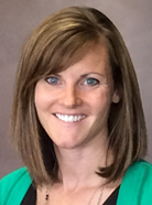 A woman with shoulder-length brown hair smiles at the camera, wearing a green cardigan over a black top, with a neutral background.